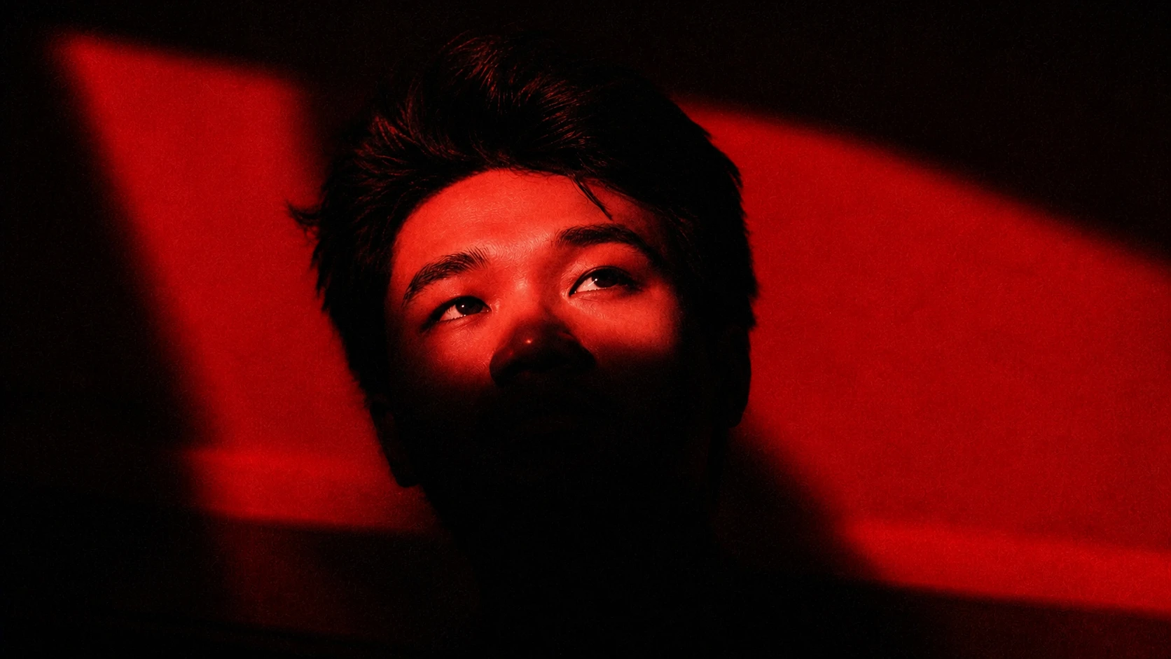 A man's face partially illuminated by dramatic red light against a dark background